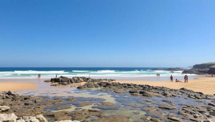 A sunny beach with clear waves, golden sands for sunbathing, rocky outcrops for exploration, accessible ramps, and diverse people enjoying the day under a blue sky.